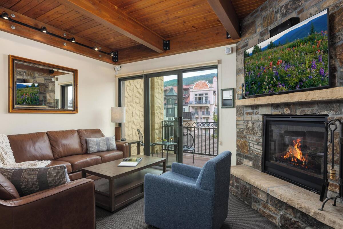A cozy living room with a stone fireplace, leather sofa, and a large TV mounted on the wall.