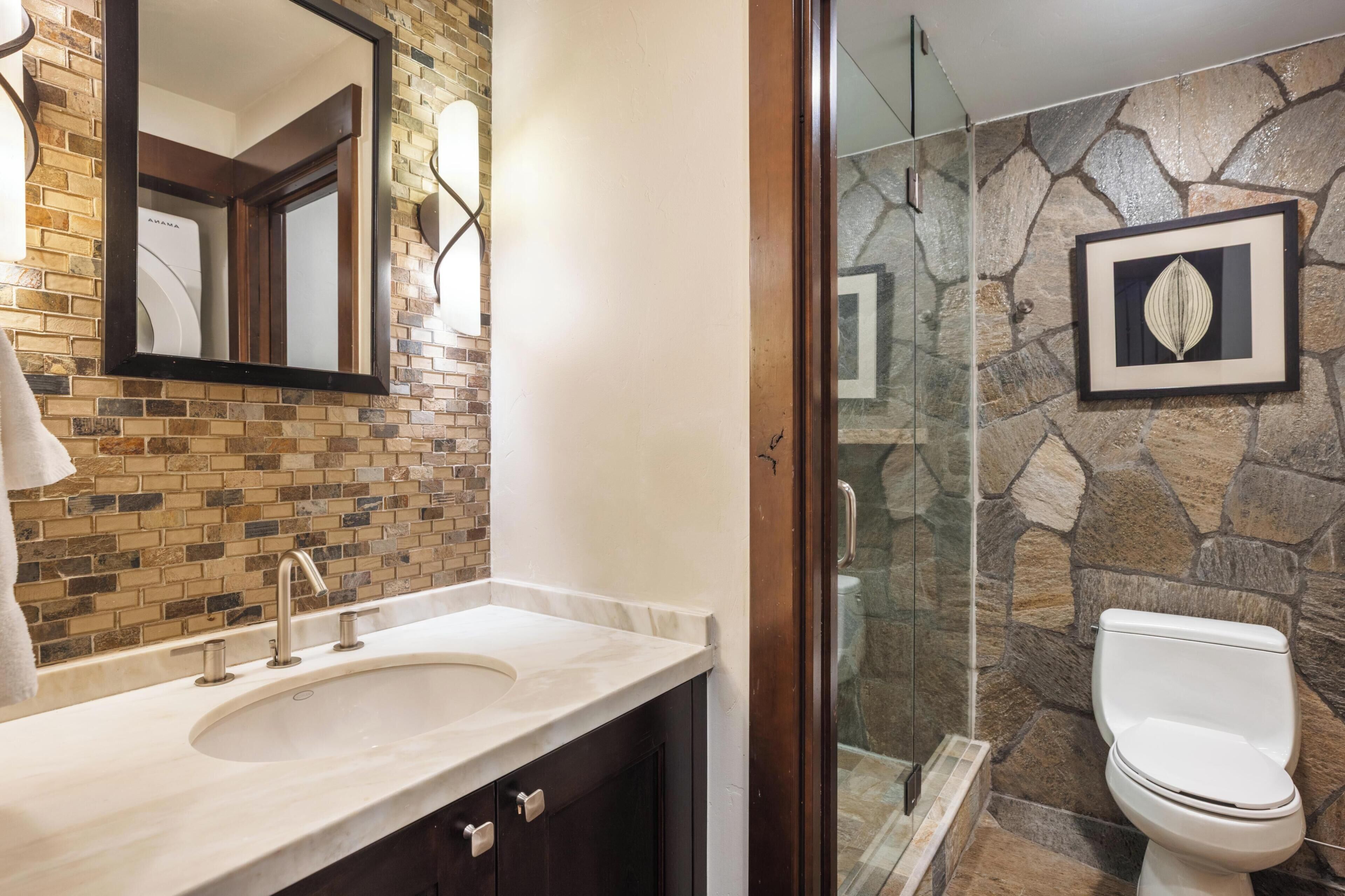A bathroom with a stone wall, a sink with a mirror, and a toilet.