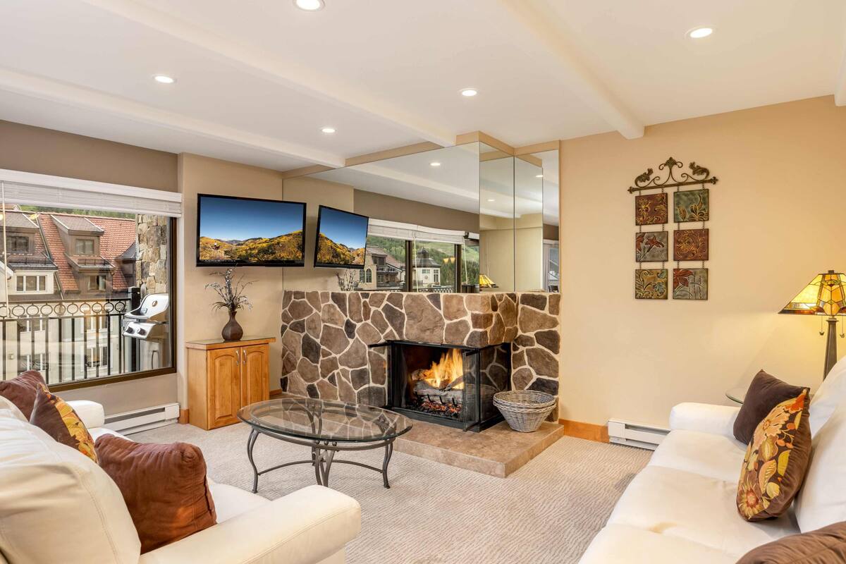 A living room with a stone fireplace, a glass coffee table, and a white sofa.