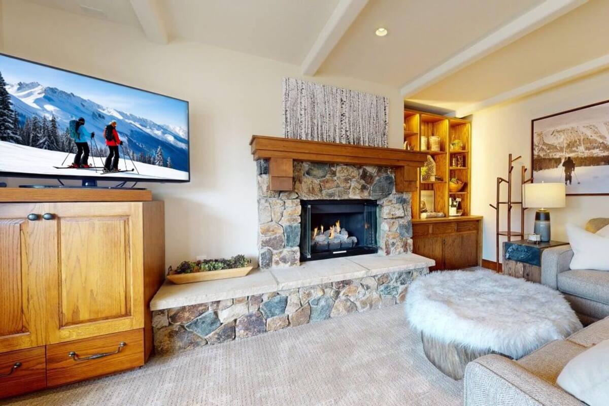 A cozy living room with a stone fireplace, a television mounted on the wall, and a sofa.