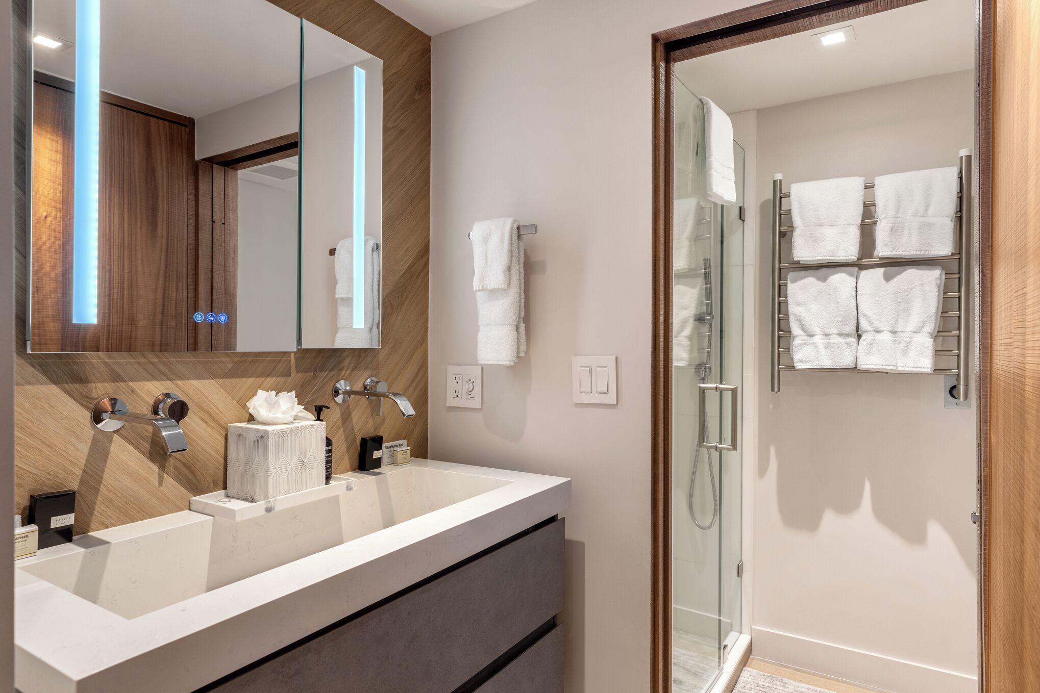 A modern bathroom with a large mirror, two sinks, a glass shower enclosure, and neatly arranged towels.