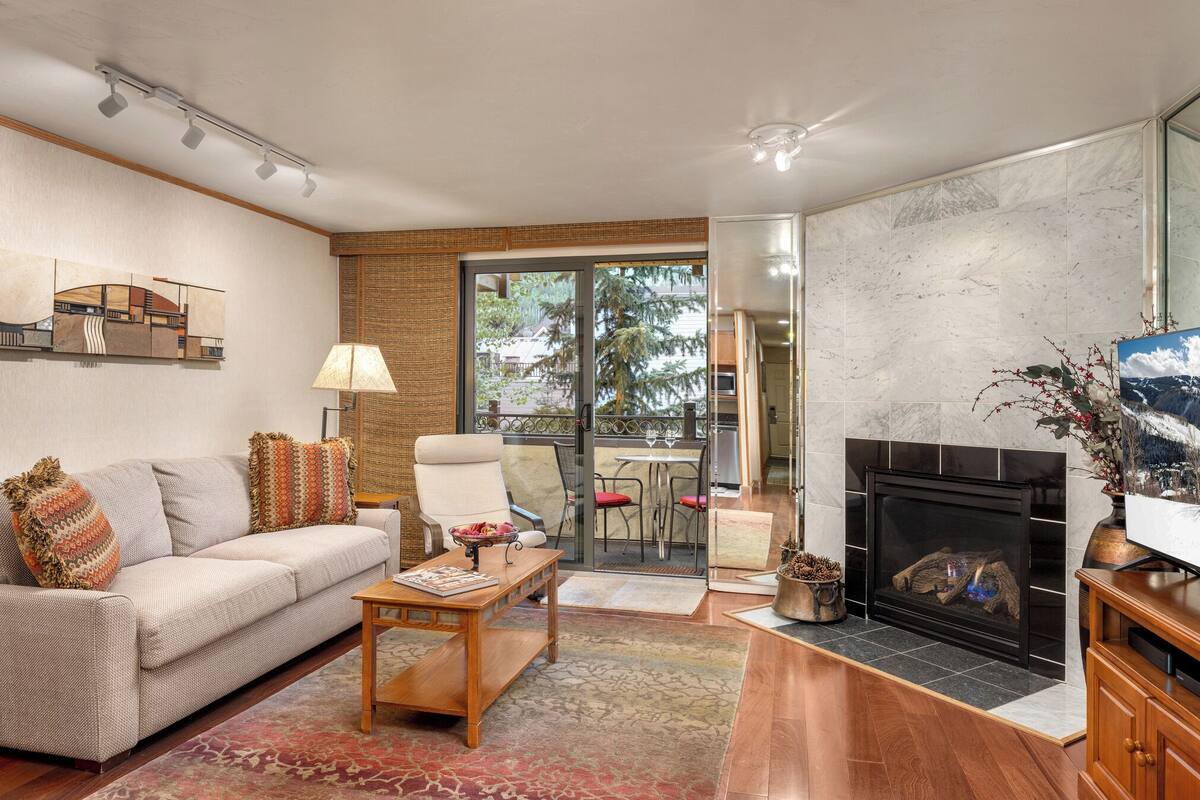 A living room with a sofa, coffee table, fireplace, and a view of the outdoors through a glass door.