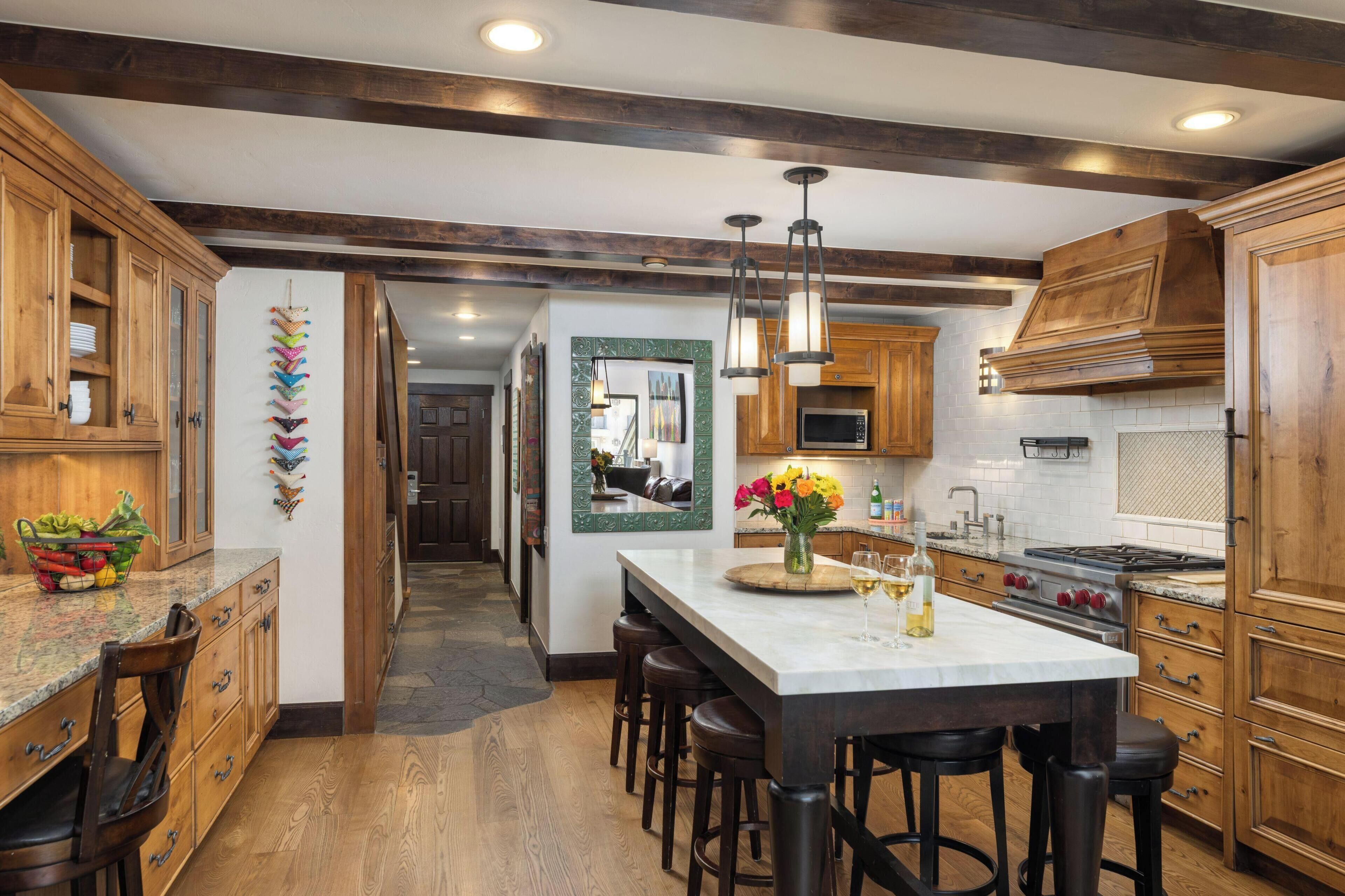 A modern kitchen with wooden cabinets, a marble island, bar stools, and a central island with a vase of flowers.
