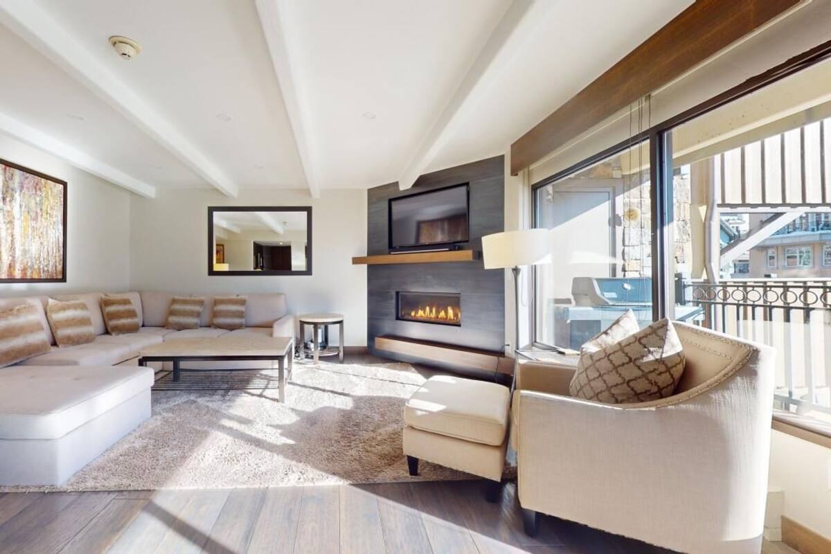 A modern living room with a sofa, armchair, fireplace, and large windows.