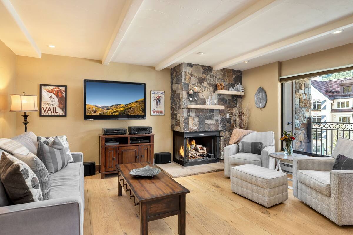 A cozy living room with a stone fireplace, comfortable seating, and a television on the wall.