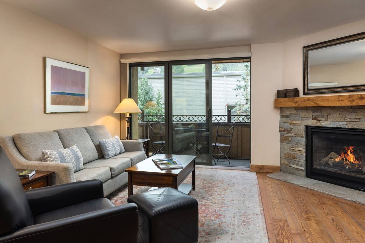A living room with a fireplace, a sofa, a coffee table, and a view of the outdoors through a sliding glass door.