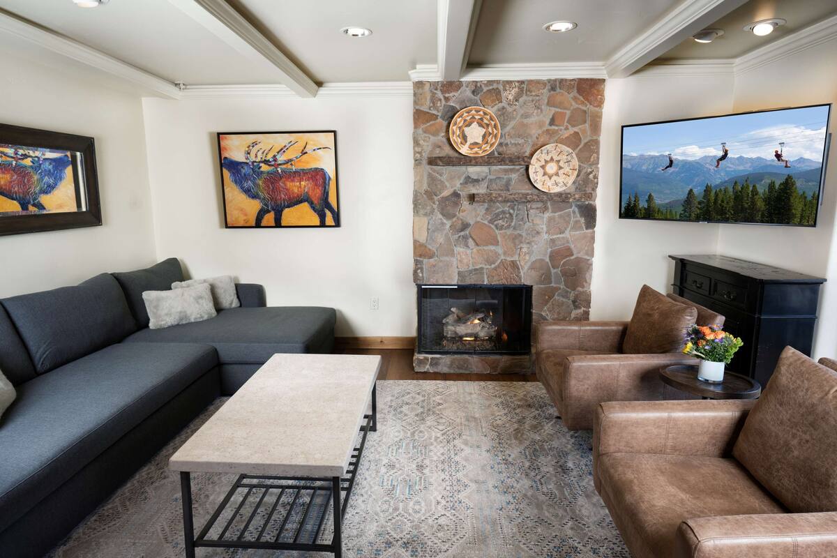 A living room with a stone fireplace, a large flat-screen TV, and artwork on the walls.