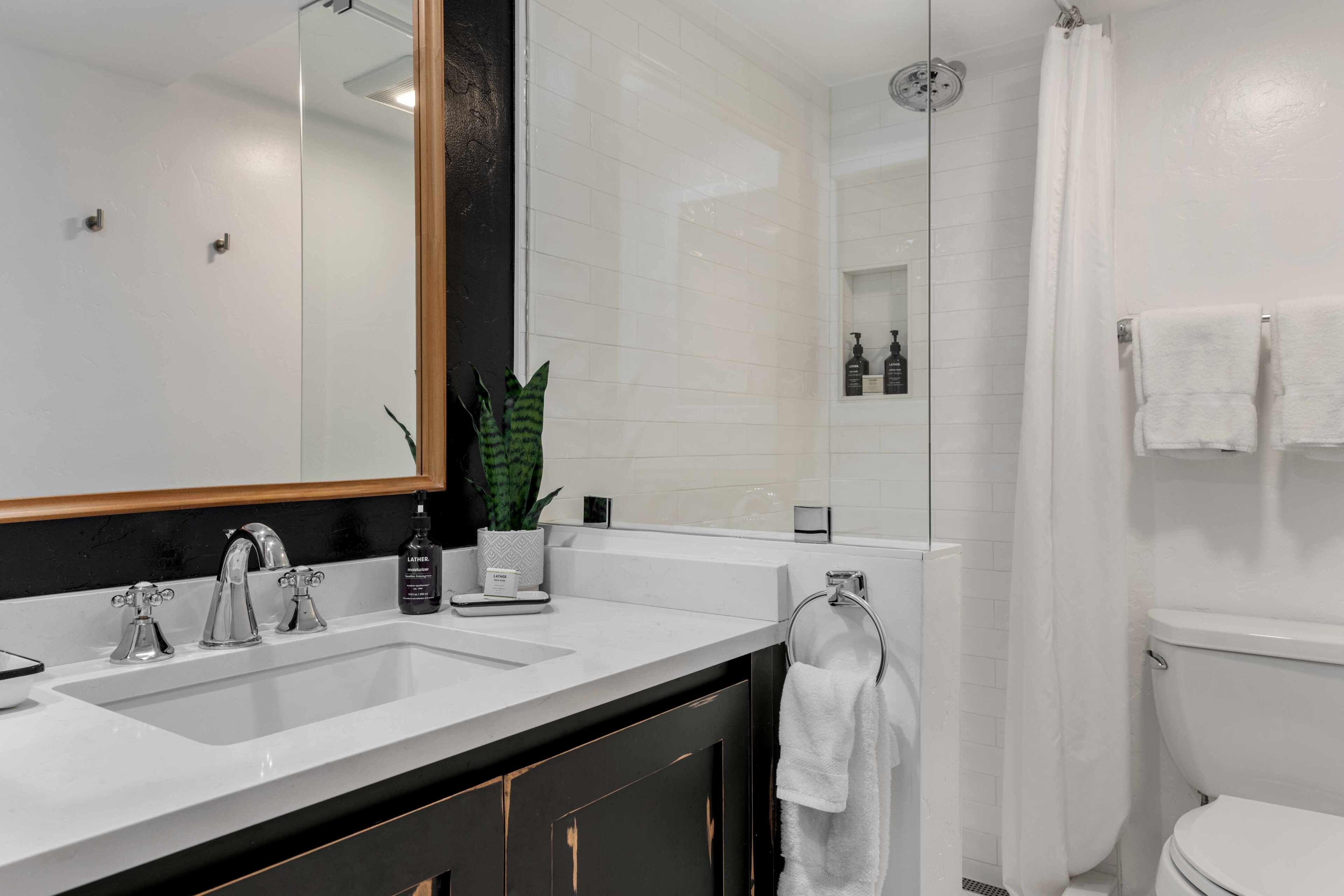 A modern bathroom with a double sink, a large mirror, a shower with a glass door, and a toilet.