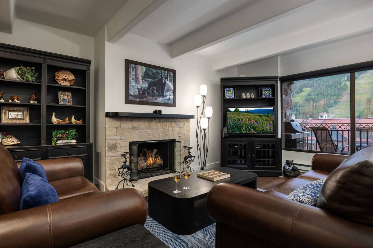 A cozy living room with leather sofas, a fireplace, and a large window offering a scenic view.