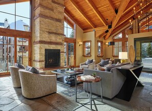 A spacious living area with a fireplace, comfortable seating, and large windows offering views of the outside. - The Landmark (Vail)