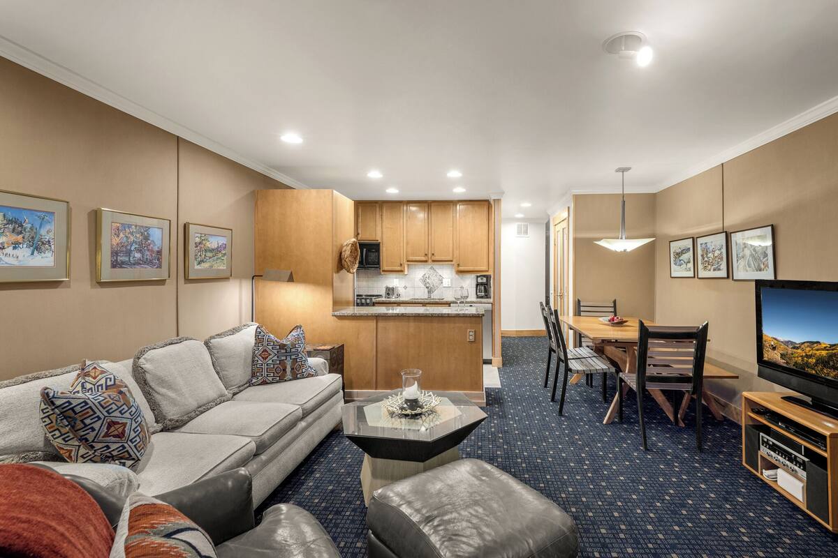A modern hotel room with a living area, kitchenette, dining space, and a TV.