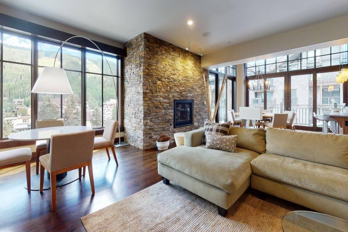 A spacious living room with a stone fireplace, large windows, and a cozy seating area.