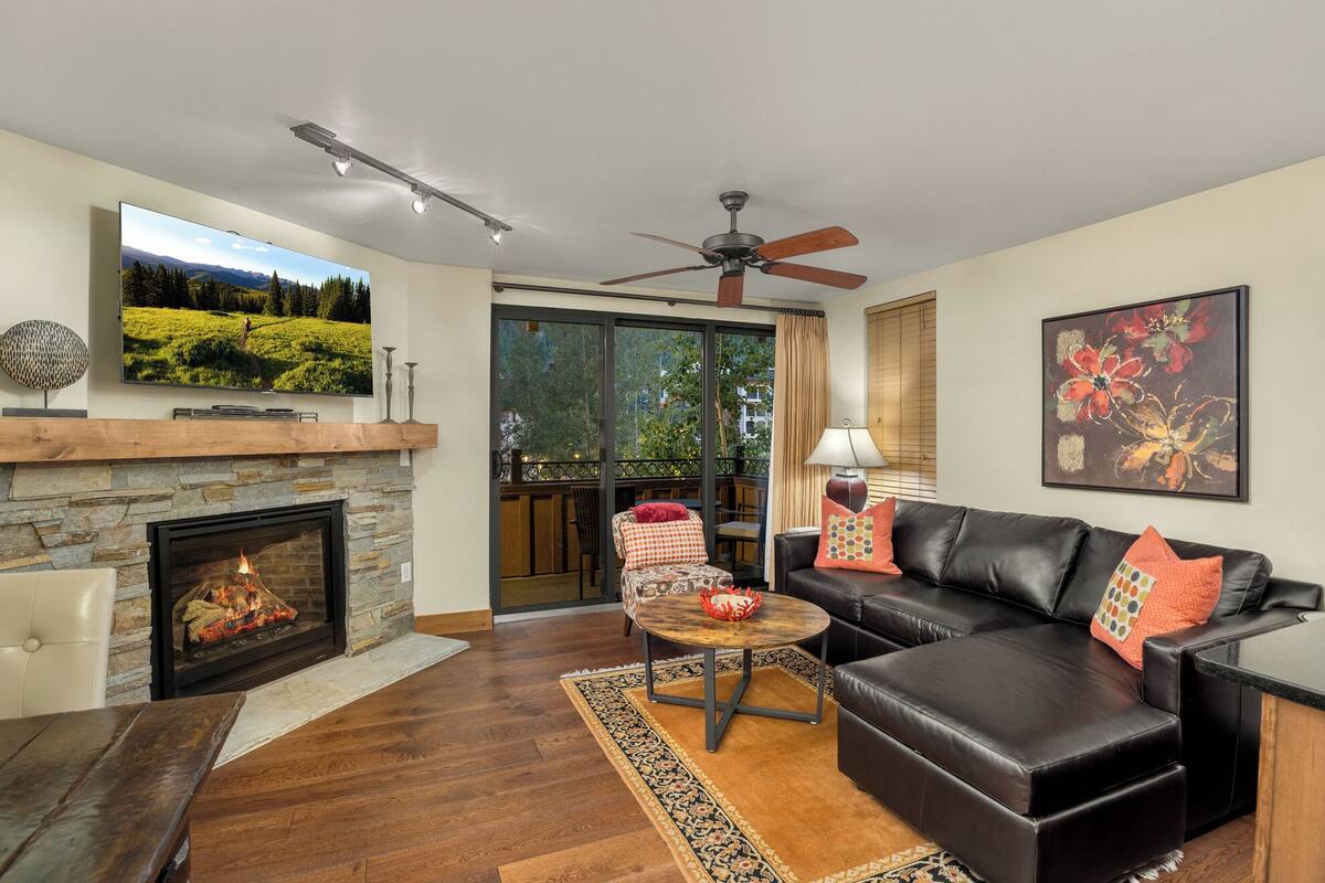 A living room with a fireplace, leather sofa, and a television mounted on the wall.