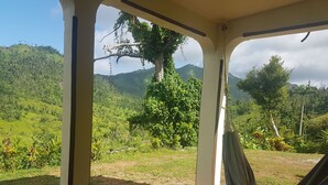A covered outdoor area with a hammock, a view of a lush green landscape, and a tiled floor. - Serenity Lodges Dominica (Marigot)