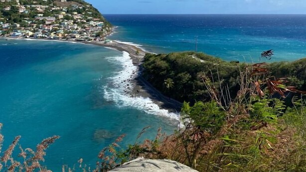 A coastal town with a rocky shoreline, clear blue sea, and a view of the ocean extending to the horizon. - Serenity Lodges Dominica (Marigot)