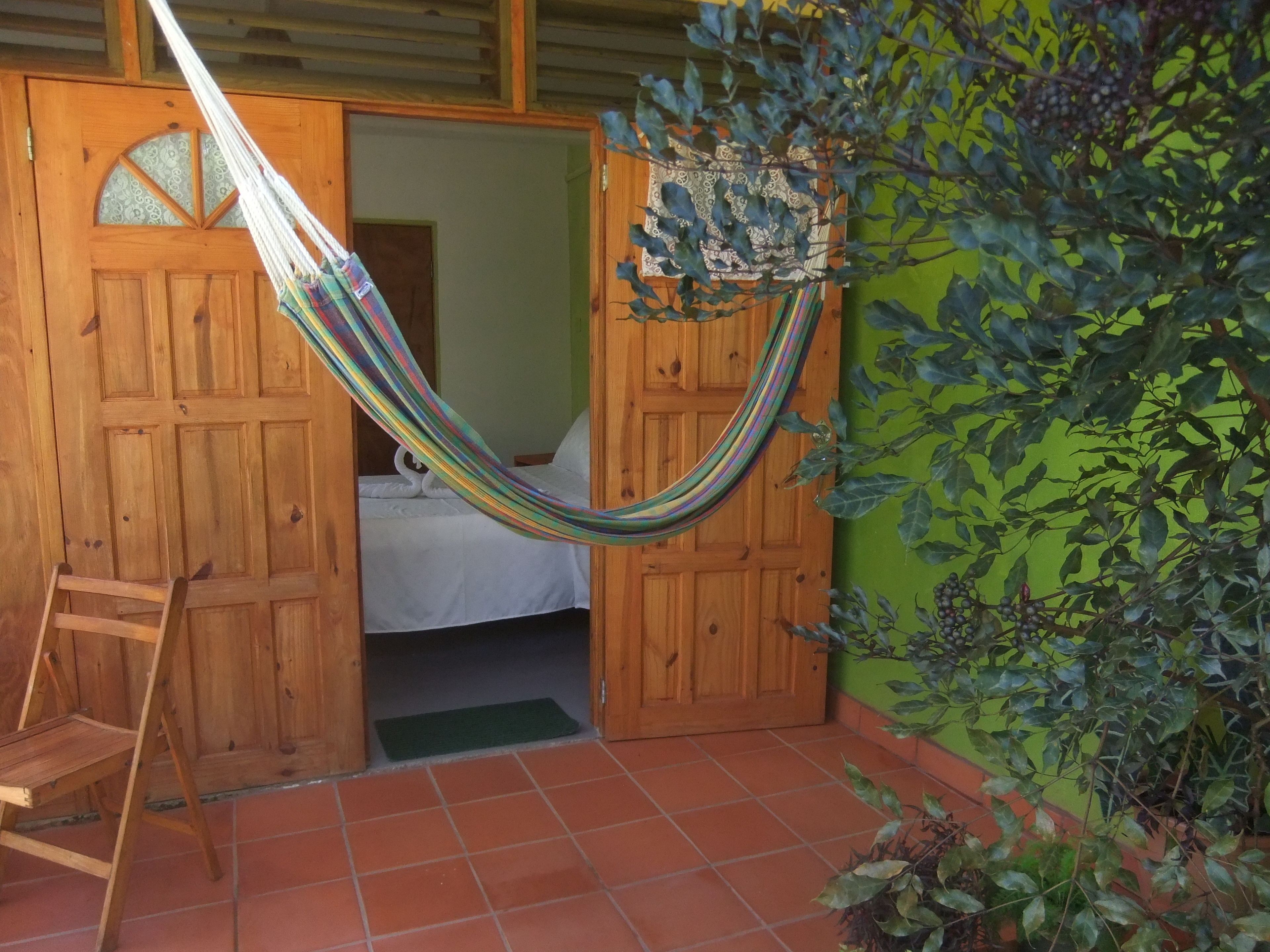 Una hamaca atada entre dos puertas de madera, una escalera de madera y una cama con colchón y almohadas blancos.