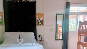 A hotel room with a bed, a nightstand, a mirror, a window with curtains, and a wooden chair. - Serenity Lodges Dominica (Marigot)