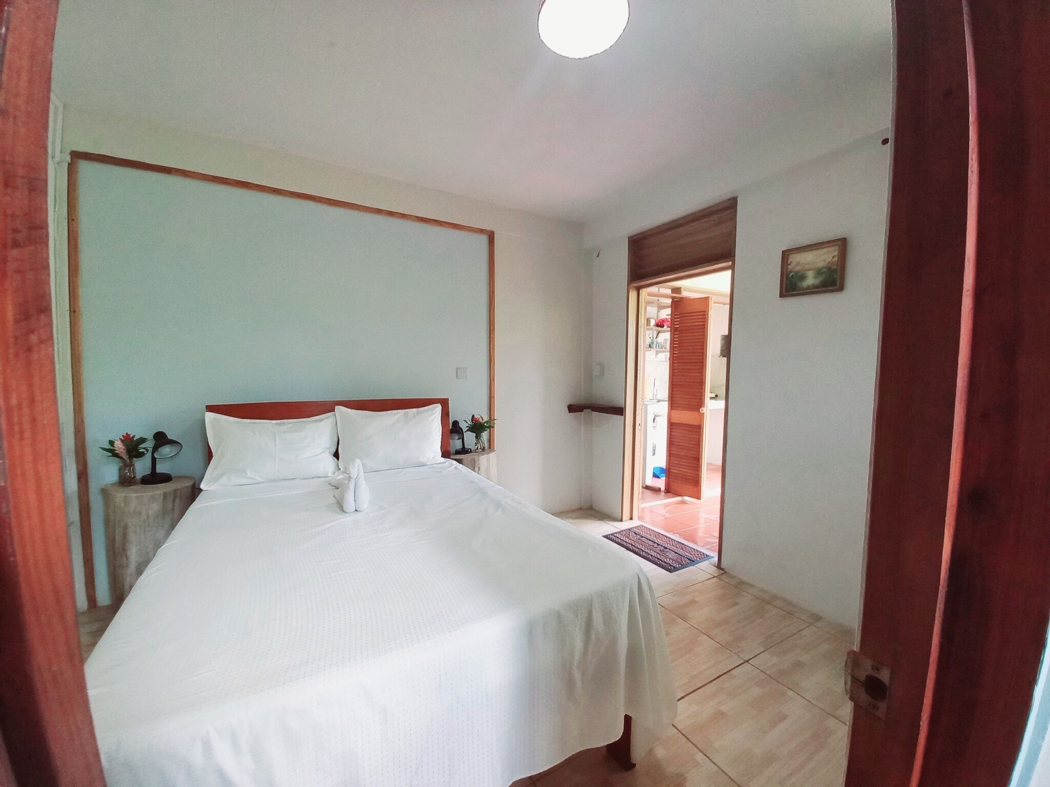Una cama bien hecha en una habitación con cabecera de madera, una mesita de noche con lámpara y una planta pequeña.