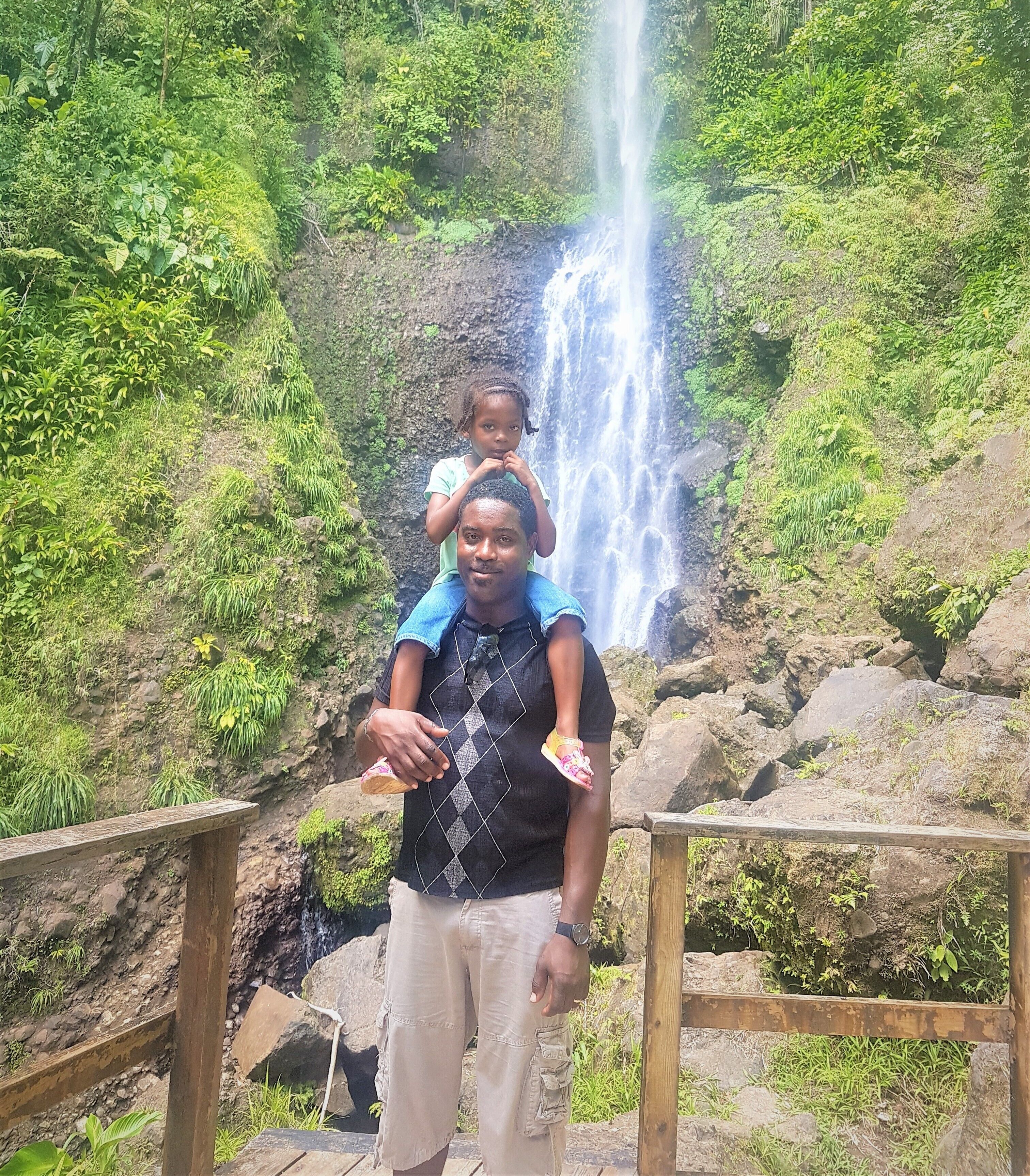 Um homem carregando uma criança em frente a uma cachoeira.