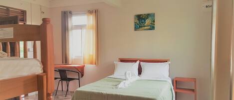 A room with a bed, a desk, and a chair. There is a window with curtains, a painting on the wall, and a tiled floor.
