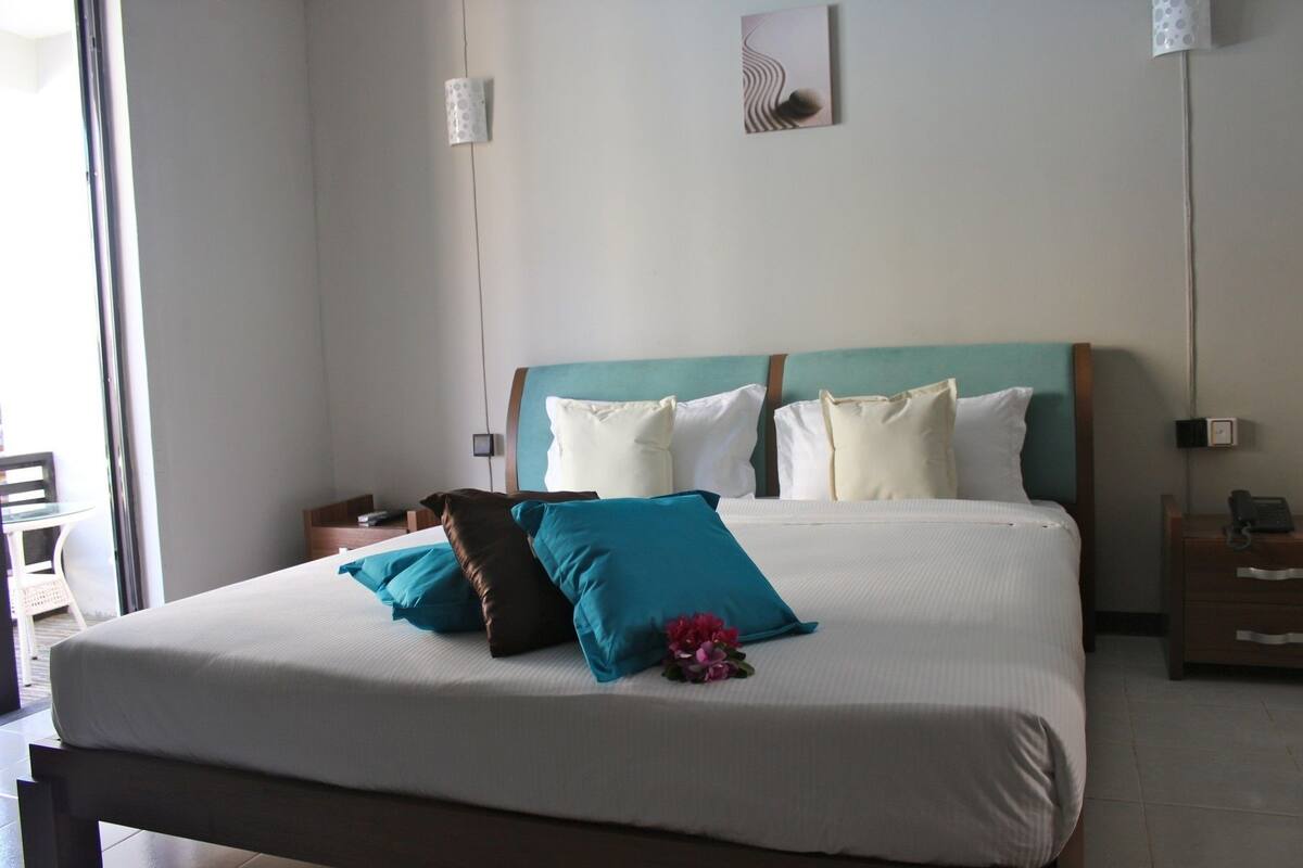 A neatly made bed with white and teal bedding, a wooden headboard, and a small decorative item on the bed.