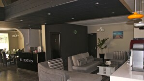 A modern reception area with a reception desk labeled "RECEPTION," a grey sofa with striped pillows, and a small coffee table. - West Palm B&B Inn (Flic-en-Flac)