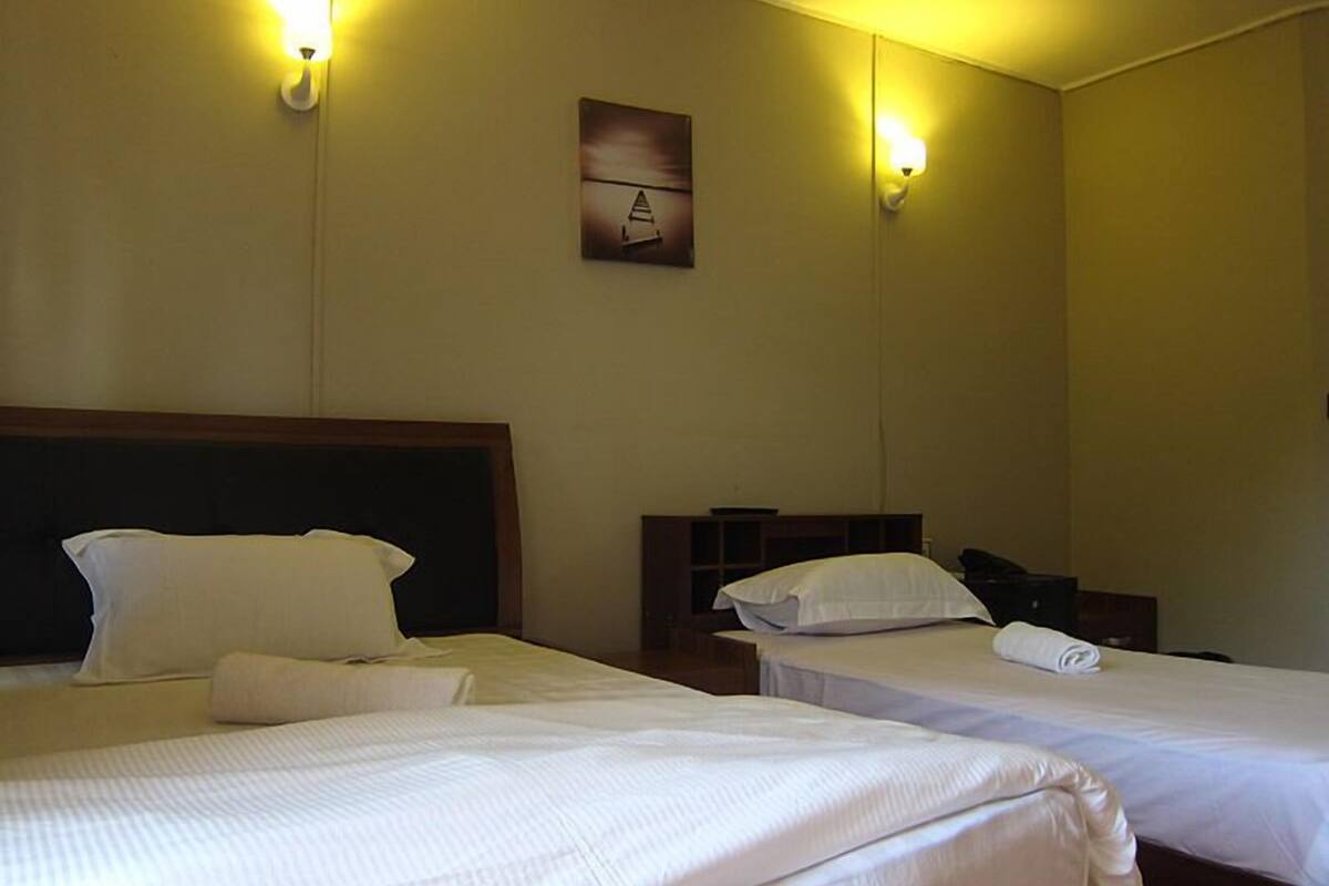 A hotel room with two beds, each with white linens and pillows, a wooden headboard, and a small bedside table with a lamp.