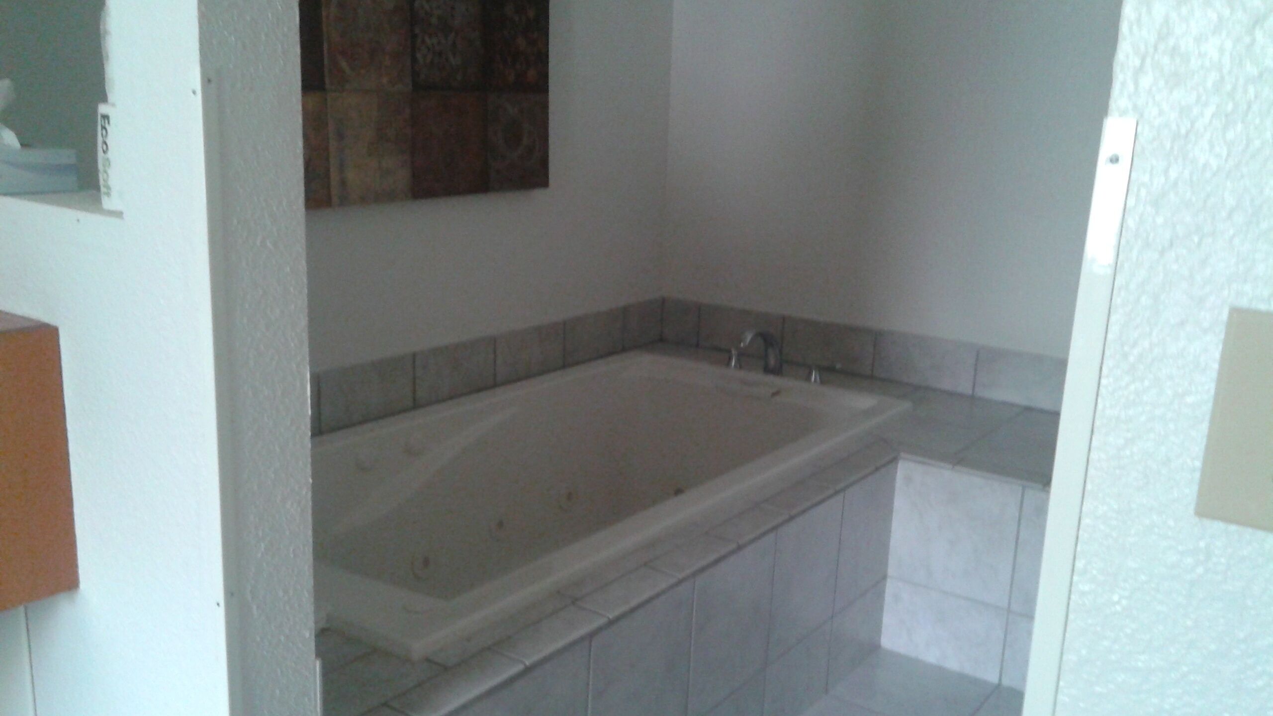 Un baño con una bañera grande, paredes de azulejos y una pequeña encimera con un espejo.