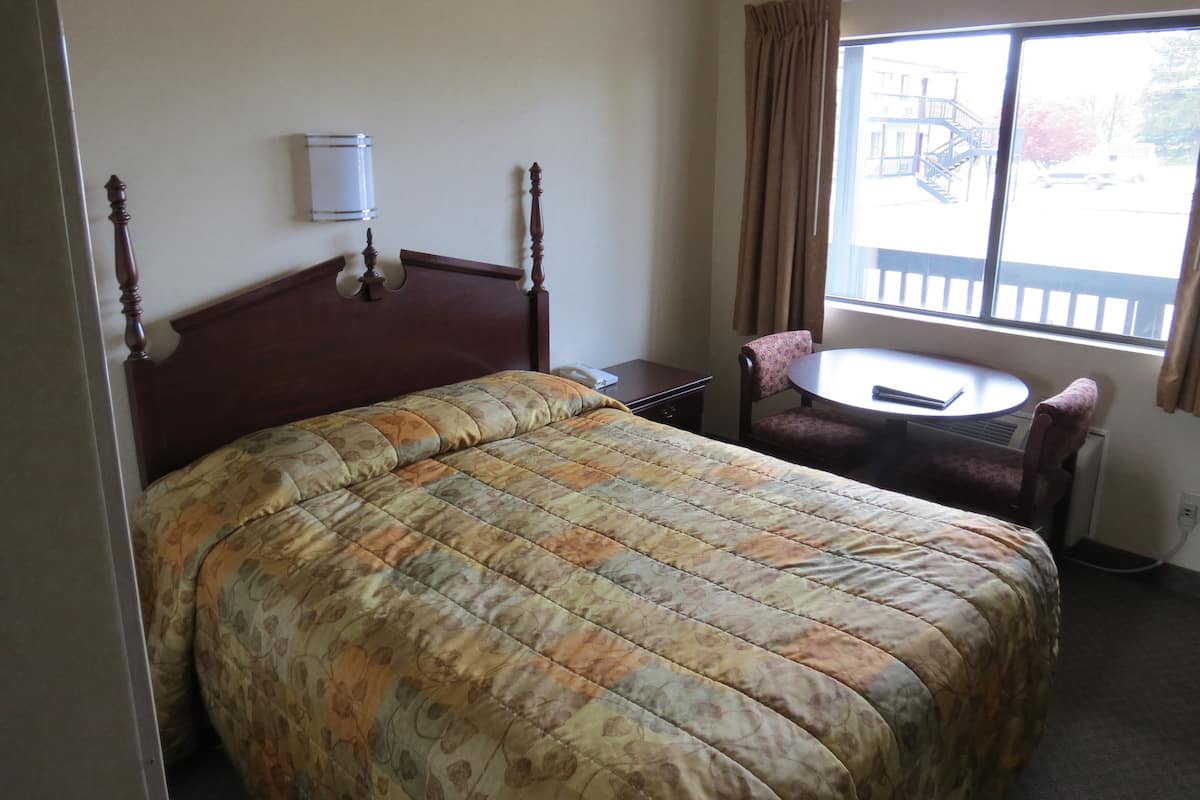 Une chambre d’hôtel avec un grand lit, une petite table, une chaise et une fenêtre donnant sur un bâtiment à l’extérieur.