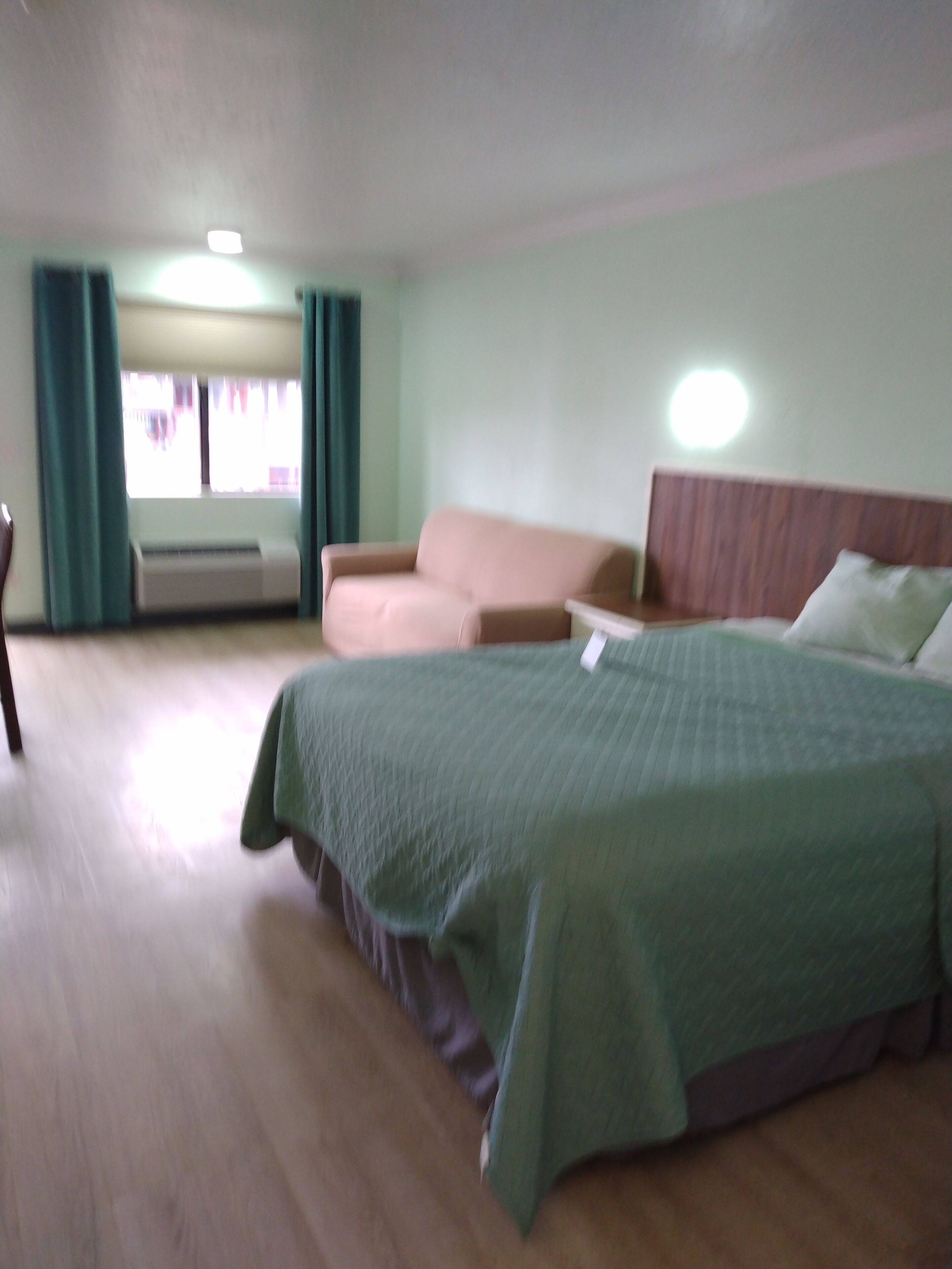 Una habitación de hotel con cama, sofá, una mesita y ventana con cortinas.