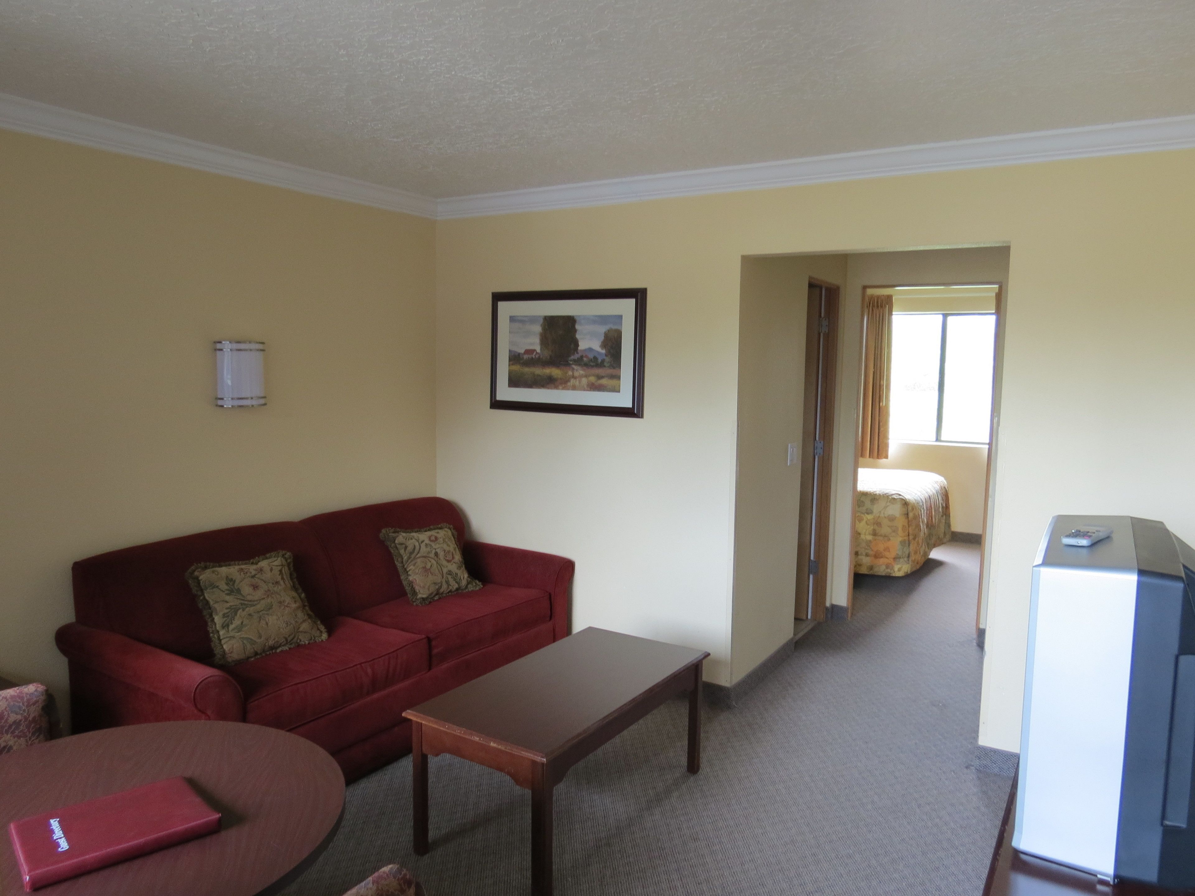 A hotel room with a red sofa, a small wooden table, a TV, and a painting on the wall.