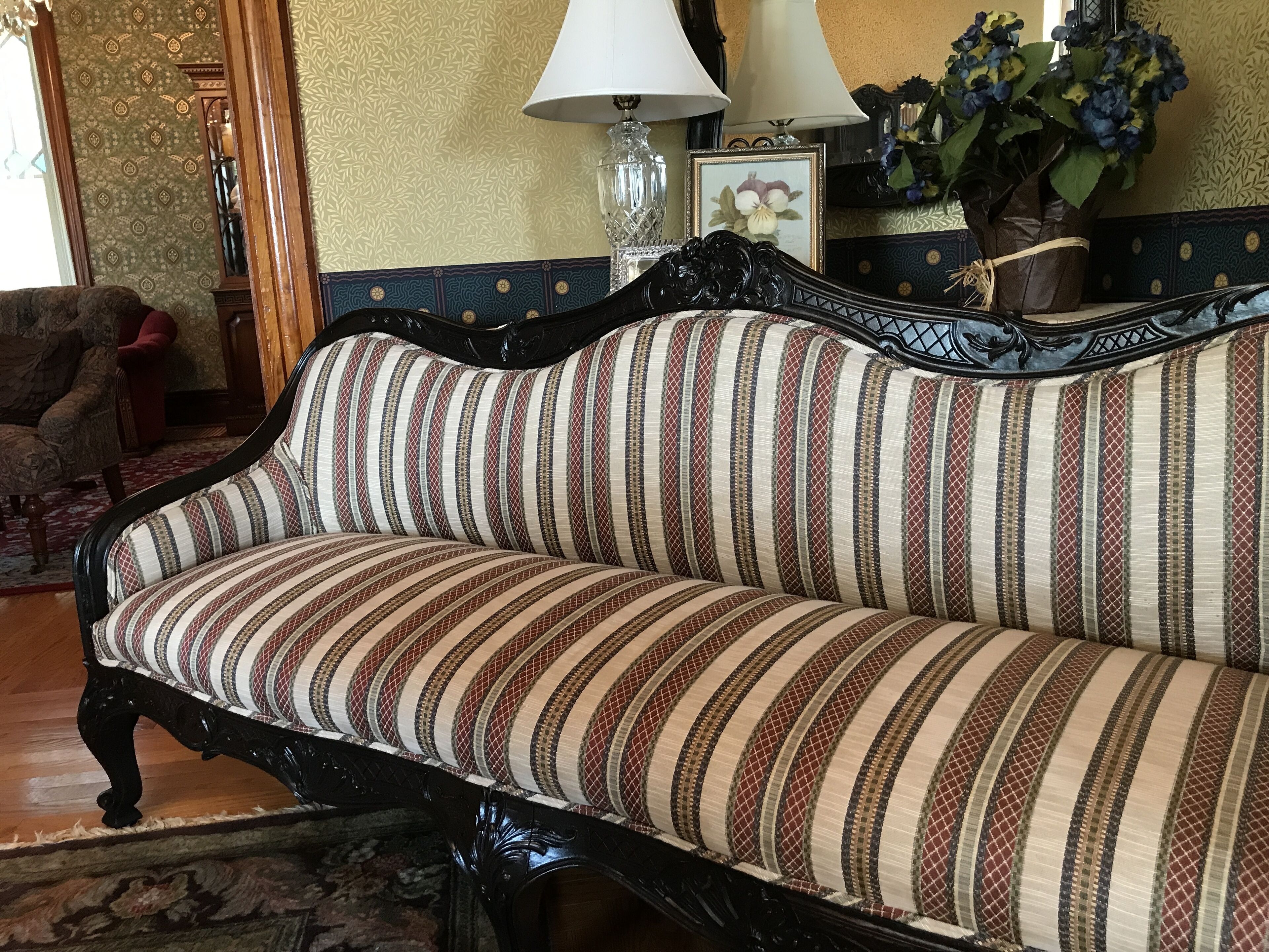 A vintage sofa with striped upholstery, a dark wooden frame, and a patterned wall in the background.