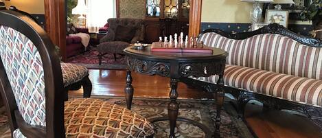 Un salón tradicional con un sillón estampado, un sofá a rayas, una mesa redonda con piezas de ajedrez y una araña.