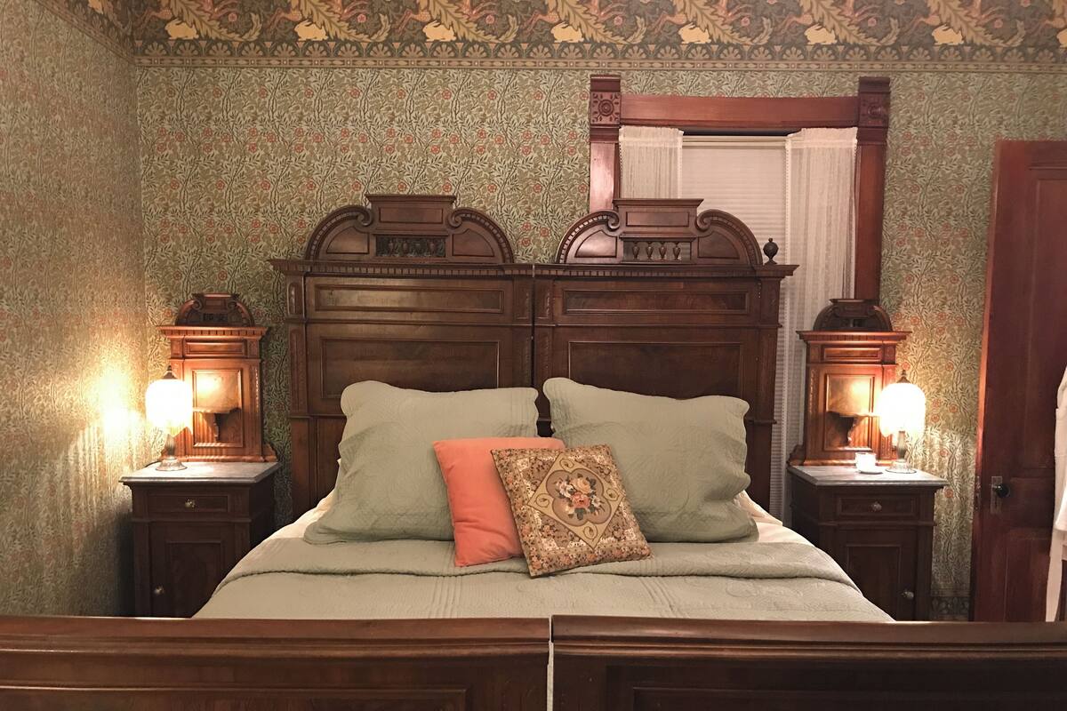 Ein traditionelles Schlafzimmer mit einem hölzernen Kopfende, zwei Nachttischlampen und floraler Tapete.