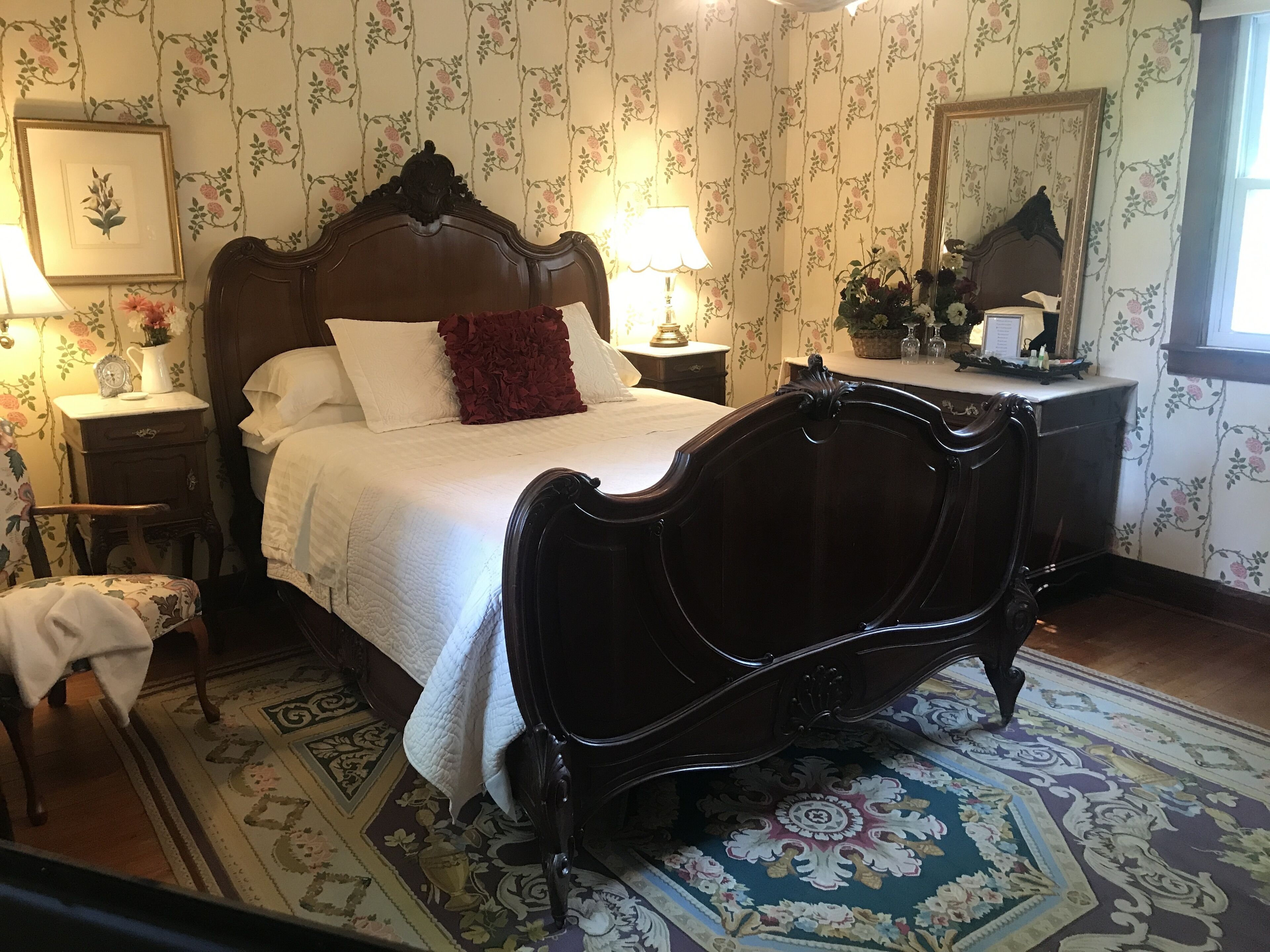 A bedroom with a large bed, a nightstand, a dresser, and a mirror.