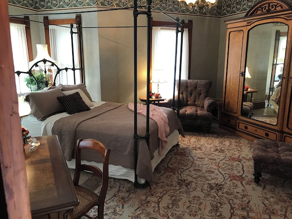 Une chambre à coucher avec un lit à baldaquin, une chaise en bois, un bureau et un grand miroir.