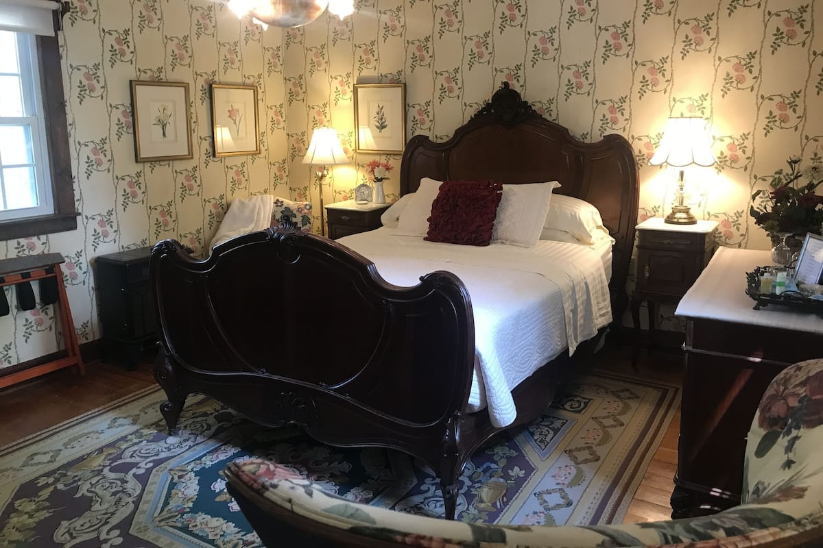 Ein klassisches Schlafzimmer mit Himmelbett, Blumenpapier und einer Chandelier.