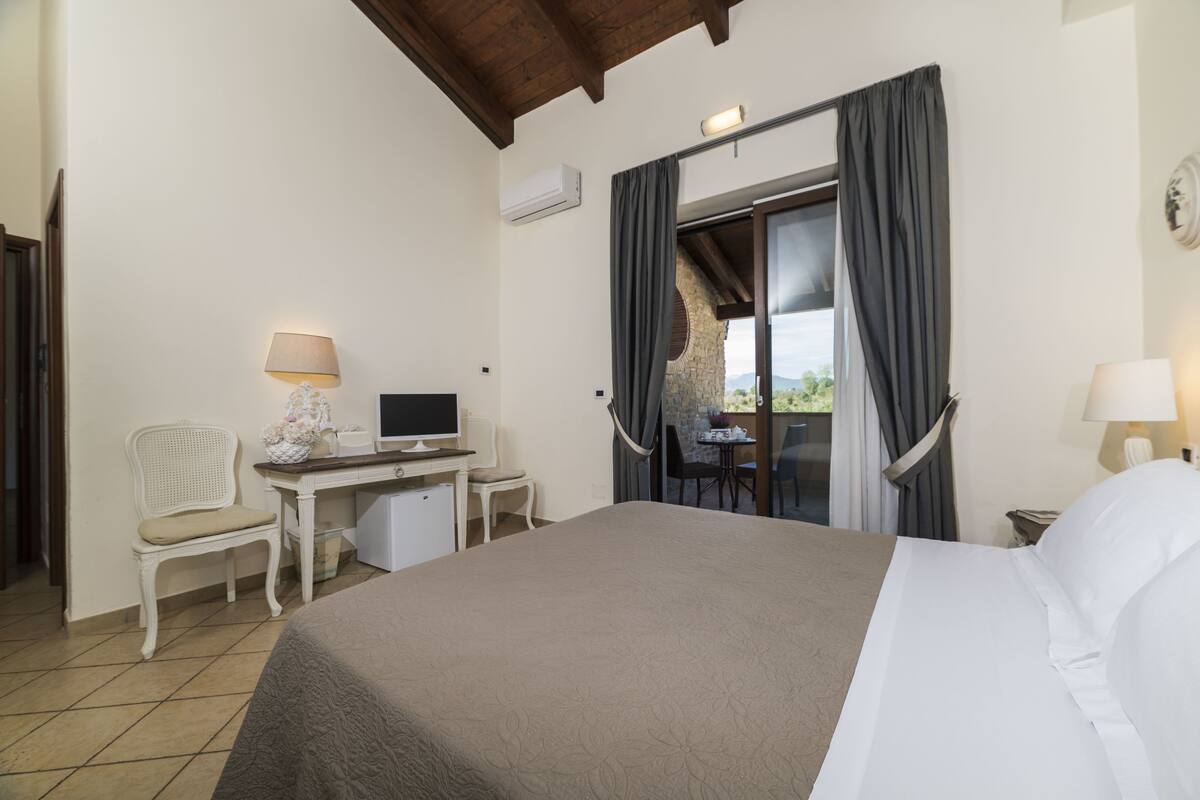 A hotel room with a bed, a desk with a computer, a chair, and a window with curtains.