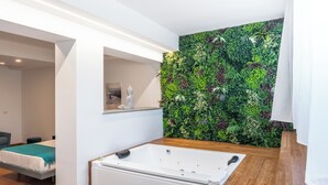 Un baño moderno con una bañera grande, un muro vertical cubierto de jardín y un tocador de madera.