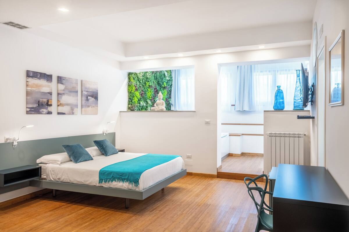 A modern bedroom with a bed, a desk, and a view of a balcony.
