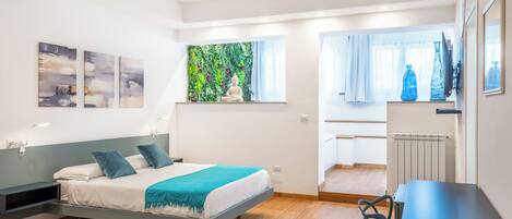 A modern bedroom with a bed, a desk, and a view of a balcony.