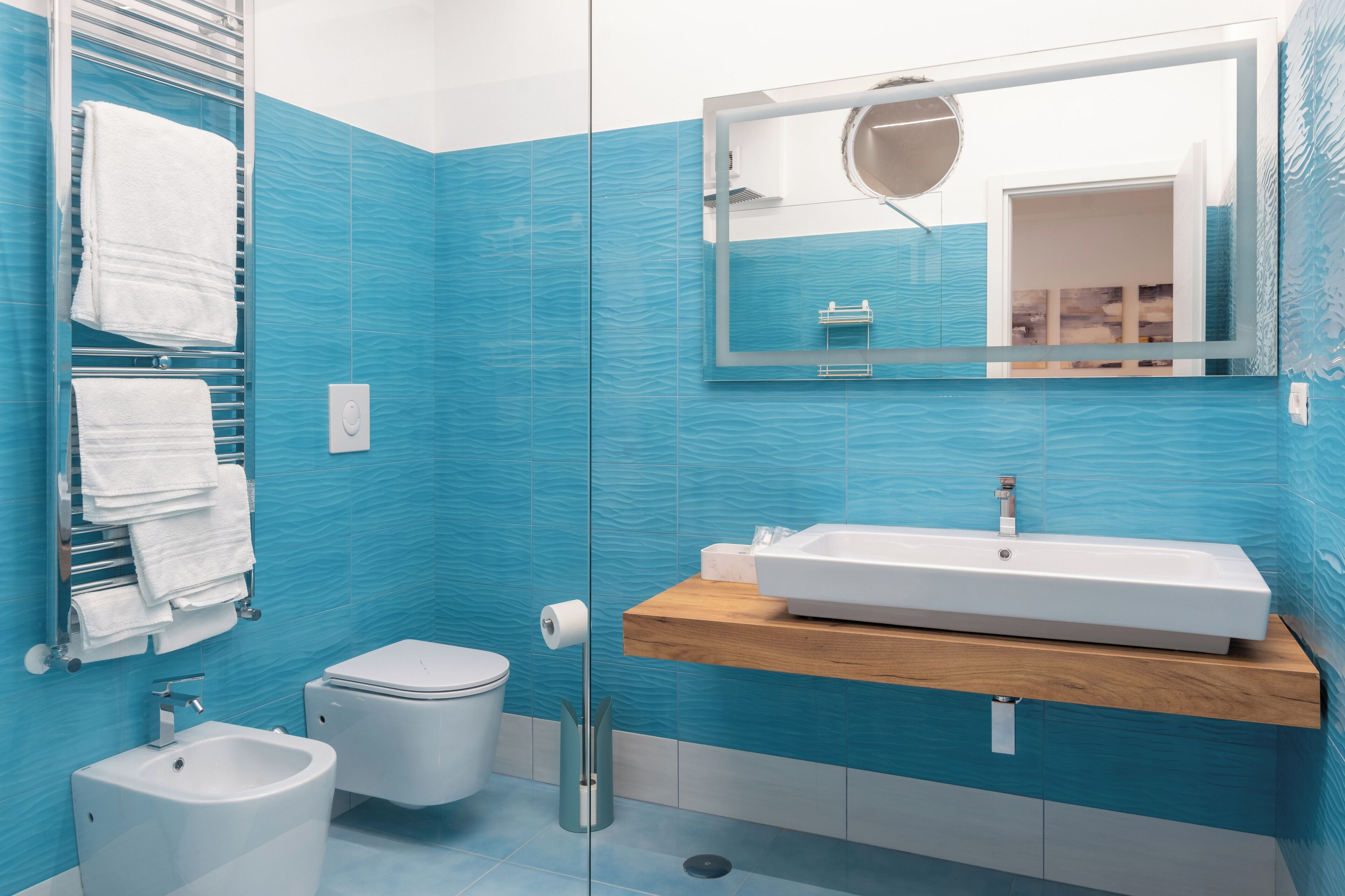 Ein modernes Badezimmer mit blauen Fliesen, einem weißen Waschbecken, einem Bidet und einer Toilette.