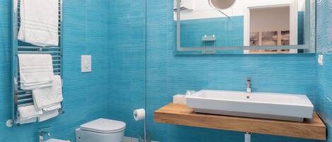 Ein modernes Badezimmer mit blauen Fliesen, einem weißen Waschbecken, einem Bidet und einer Toilette.