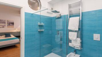A modern bathroom with blue tiles, a glass-enclosed shower, a bidet, and a towel rack.