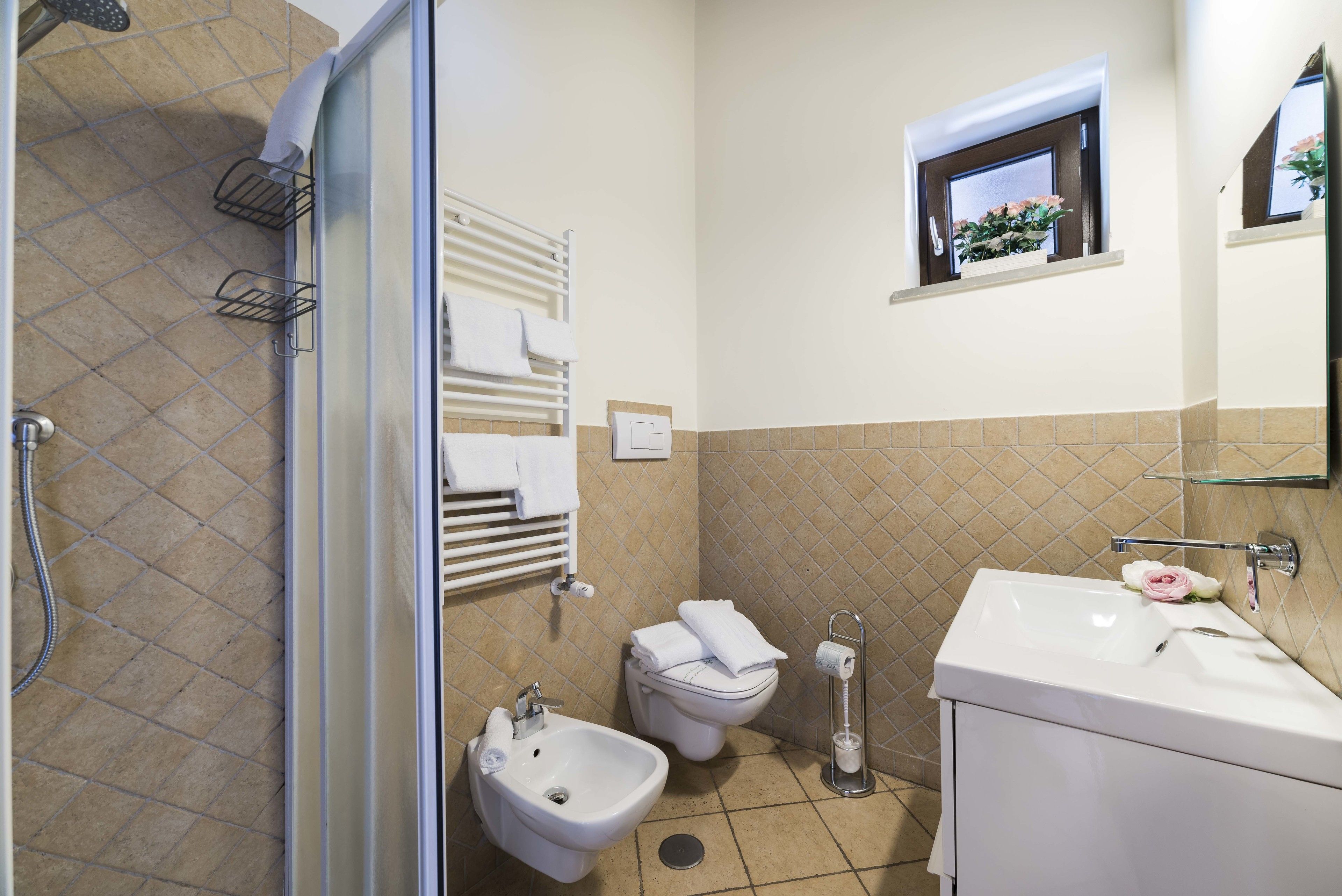 Ein Badezimmer mit Dusche, Bidet, Toilette, Waschbecken und einem kleinen Fenster mit Blumen.