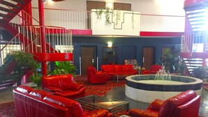 A lobby with red leather sofas, a glass coffee table, a central fountain, and a staircase.