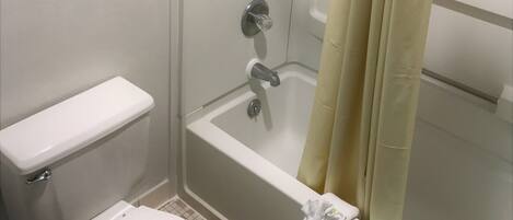 A small, enclosed bathroom with a toilet, a bathtub, and a shower.