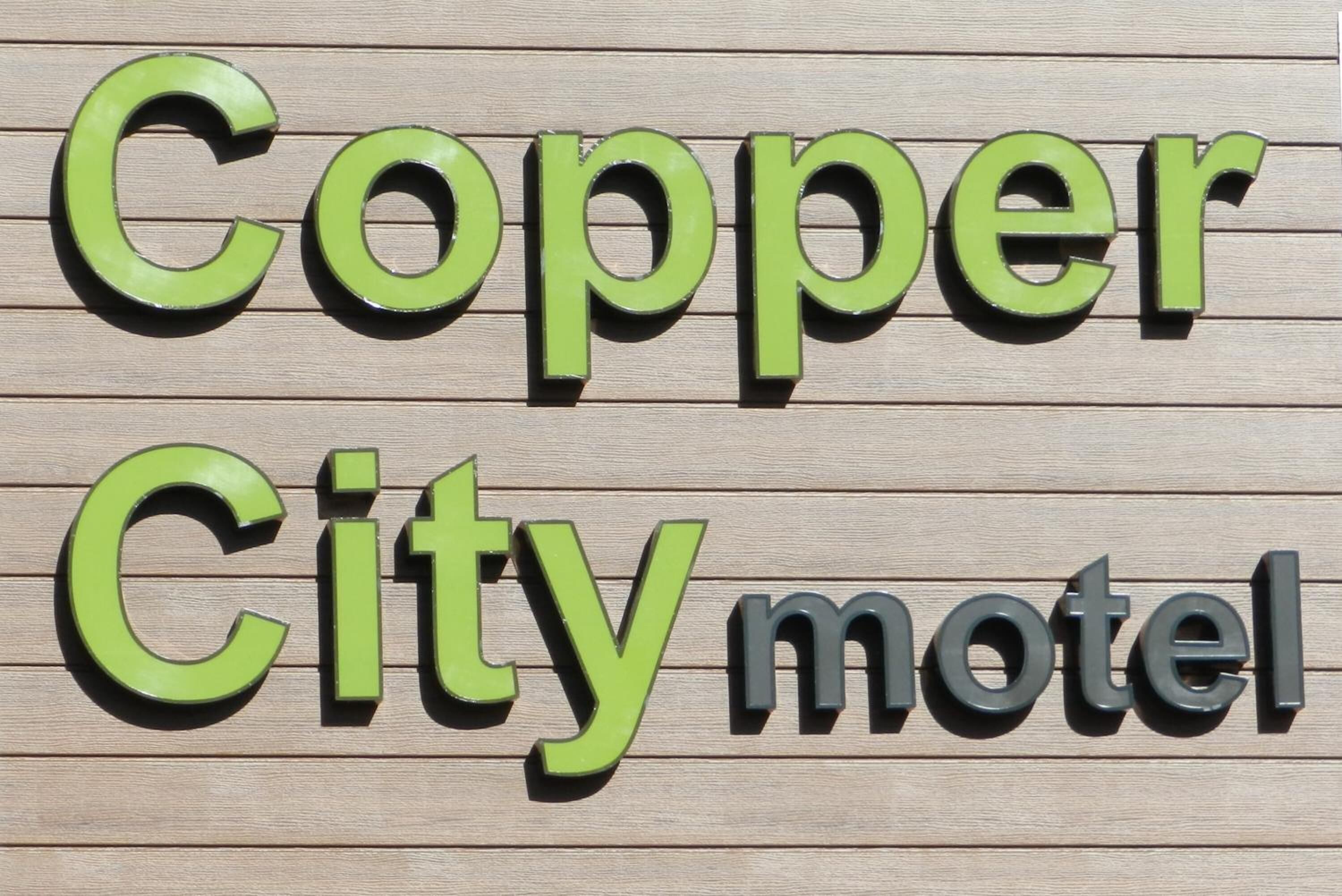 A sign with the words 'Copper City motel' in green and black letters on a wooden background.
