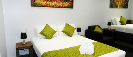 A hotel room with a large bed, two bedside tables, a sofa, and two paintings on the walls.