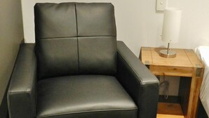 A black leather armchair in a hotel room with a wooden nightstand and a bedside table. - Copper City Motel (Pioneer)